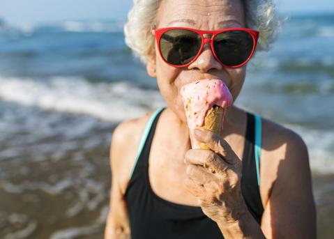 Ältere Frau mit Sonnenbrille isst Eis am Strand