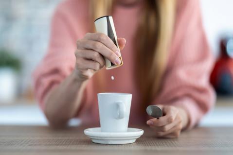 Frau gibt Süßstoff in Kaffeetasse